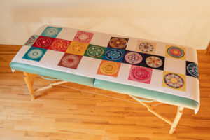 Behandlungsliege mit ausgelegter Omjaah® Veda Ur-Lichtquell 19+ Mandala-Matte – energetisches Anwendungstuch mit 19 farbigen Symbolbildern zur Förderung von Entspannung, innerer Balance und bewusster Ausrichtung